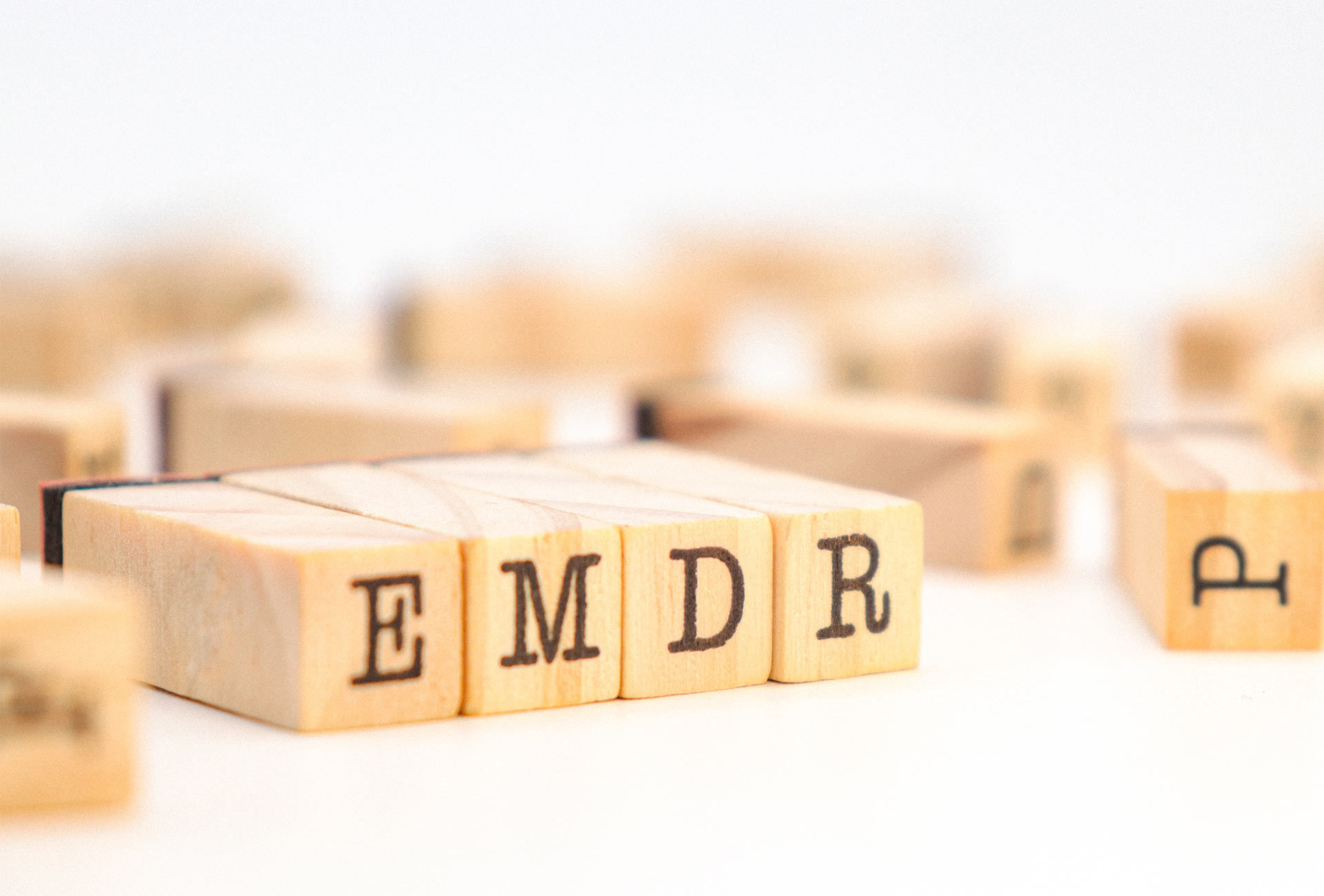 Wooden letter blocks spelling “EMDR” arranged on a white surface, symbolizing Eye Movement Desensitization and Reprocessing therapy. The image conveys the concept of healing and reprocessing traumatic memories through structured therapeutic techniques.